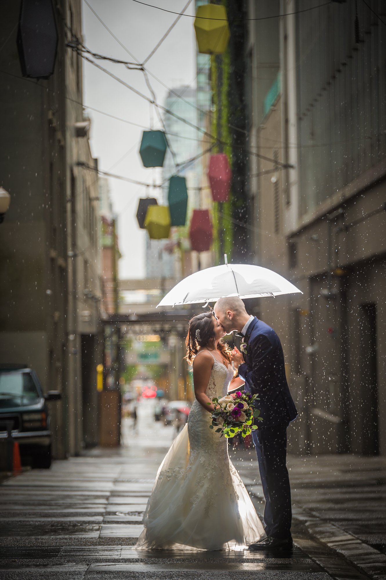 Ozzy and Jessica kissing under a white umbrella in the rain in Vancouver