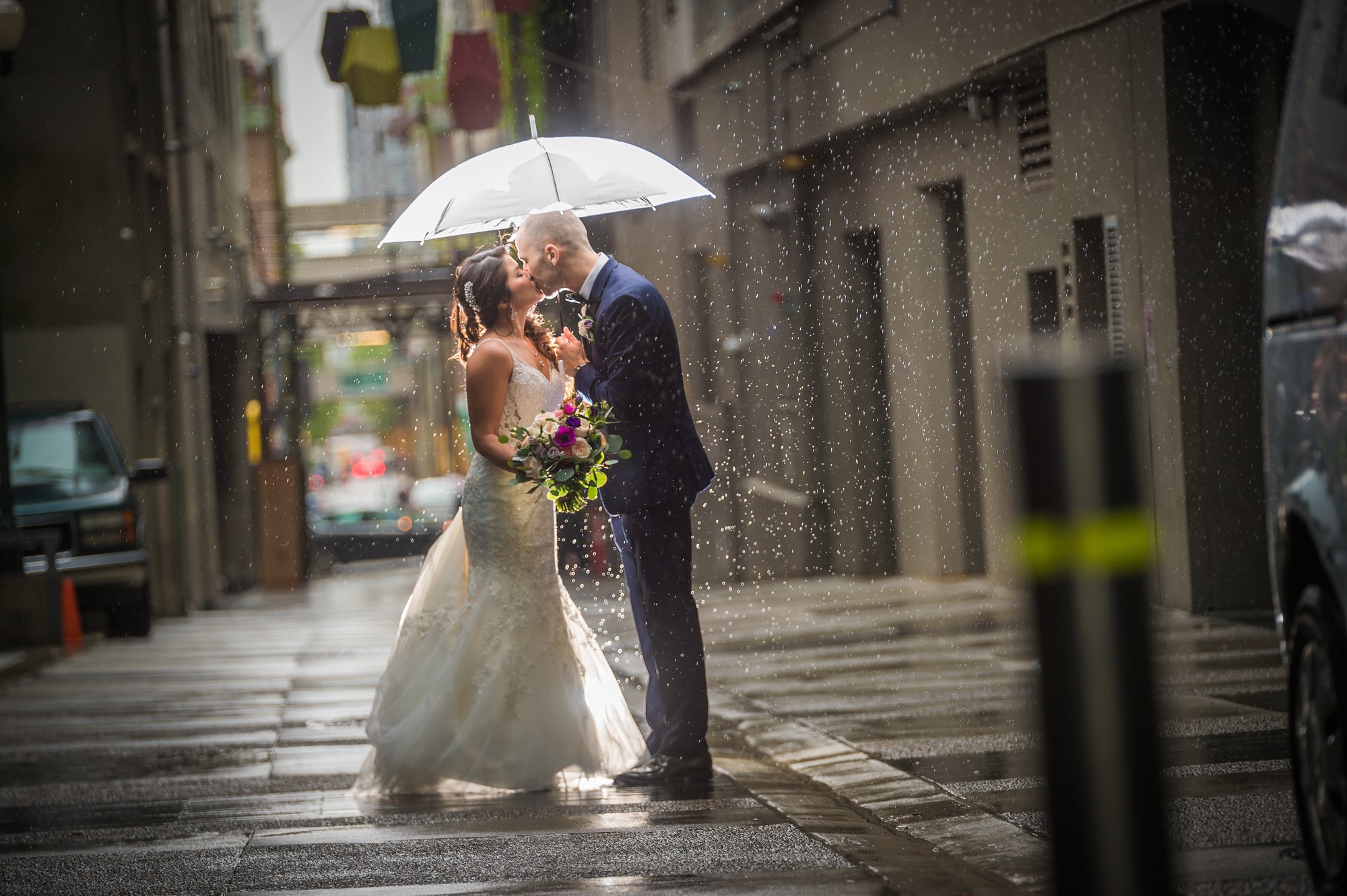 Ozzy and Jessica kissing under a white umbrella in the rain in Vancouver